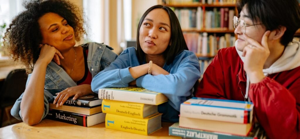 Three diverse students studying together in a university library with books around them.
