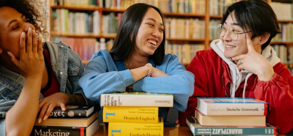 Three diverse students laughing and studying together in a cozy library setting.